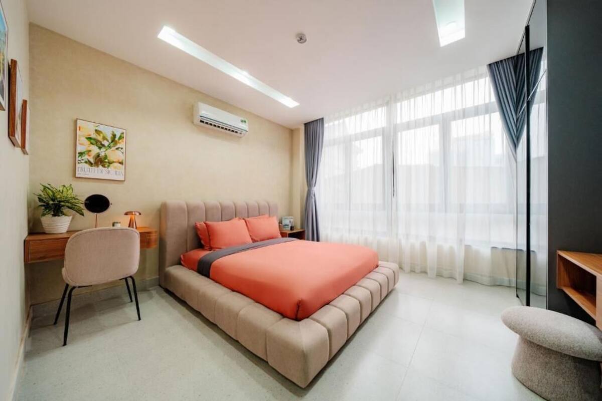 A modern bedroom with a bed, desk, chair, and a potted plant.