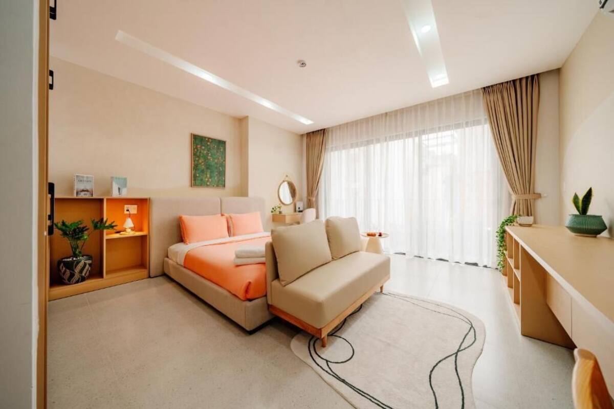 A modern hotel room with a bed, sofa, desk, and large windows.