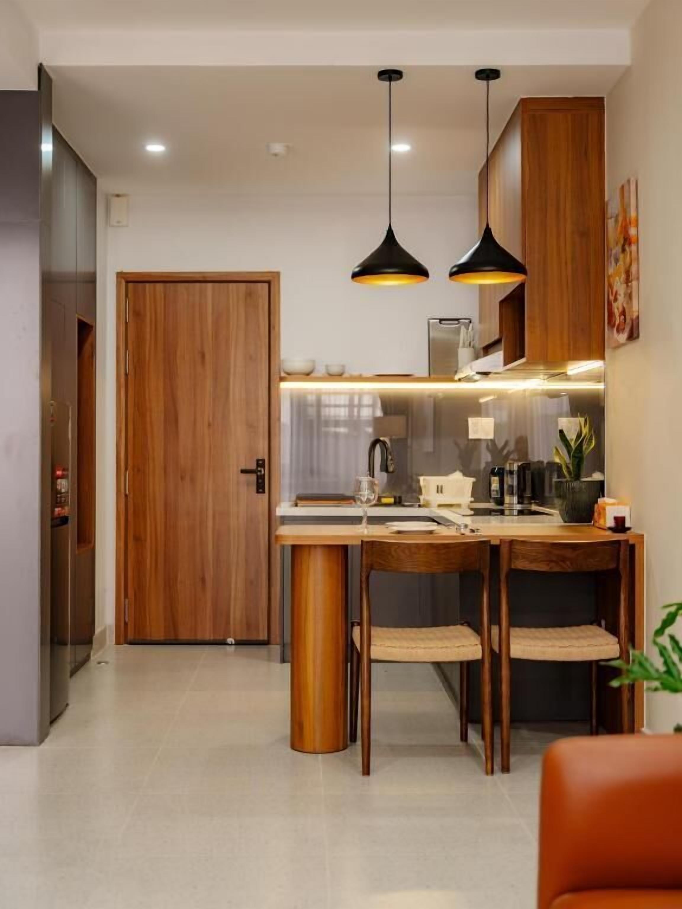 A modern kitchen with wooden cabinets, a central island, pendant lighting, and a dining area with chairs.