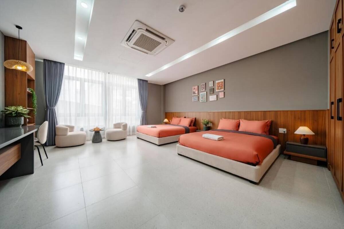 A hotel room with two beds, a desk, a chair, a small table, and a window with curtains.