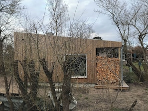 A modern wooden building with a large window and a stack of firewood outside. - Architect-designed wooden house near beach (Odder)