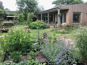 A modern house with a covered patio, garden with various plants and flowers, and a wooden exterior. - Architect-designed wooden house near beach (Odder)