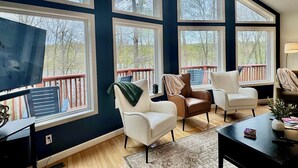 A spacious living room with large windows, a television, and multiple seating areas. - Zen at Marker 10~ Lakefront Home with Hot Tub! (Pittsville)