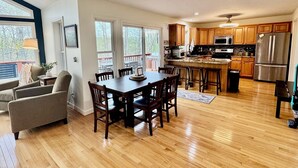 A spacious kitchen with wooden cabinets, a stainless steel refrigerator, and a dining area with a wooden table and chairs. - Zen at Marker 10~ Lakefront Home with Hot Tub! (Pittsville)