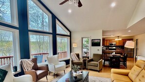 A spacious living room with a large window, a ceiling fan, and a view of the outdoors. - Zen at Marker 10~ Lakefront Home with Hot Tub! (Pittsville)