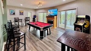 A pool table with chairs, a television, arcade games, and a fireplace. - Zen at Marker 10~ Lakefront Home with Hot Tub! (Pittsville)