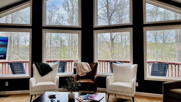A room with large windows, a fireplace, a coffee table, and two white armchairs. - Zen at Marker 10~ Lakefront Home with Hot Tub! (Pittsville)