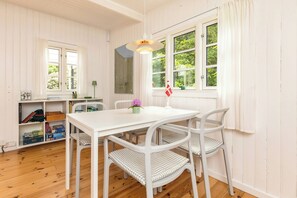 A white dining table with four chairs, a hanging light fixture, and a window with curtains.