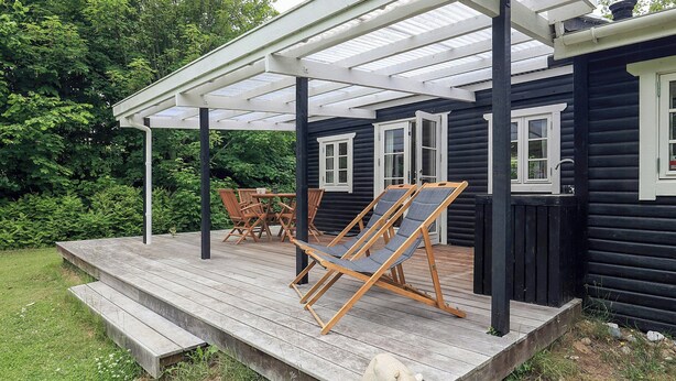 A wooden deck with a pergola, two lounge chairs, and a small table. - Cottage life in intimate wooden cabin (Dronningmølle)