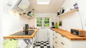 A compact kitchen with a central island, a washing machine, and a window with a view of greenery. - Cottage life in intimate wooden cabin (Dronningmølle)