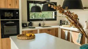 A modern kitchen with a large island, wooden cabinets, a built-in oven, and a window with a view. - Ibiza-style villa in Jávea near beach with pool (Jávea)