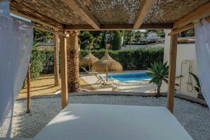 Área de piscina com pérgola, espreguiçadeiras e guarda-sóis de palha.