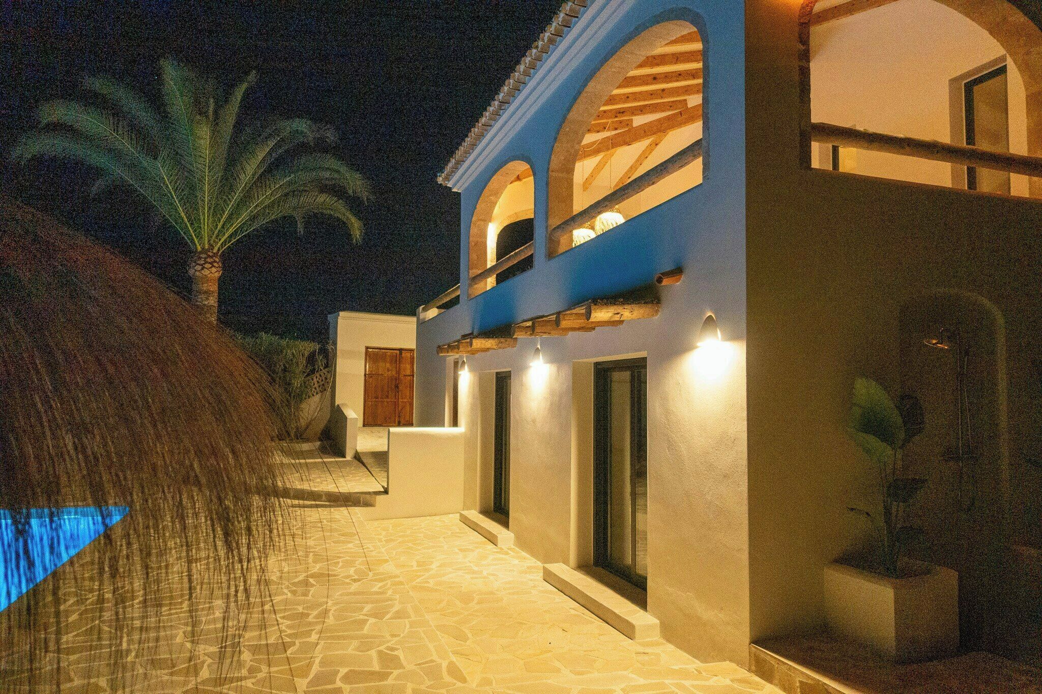 Un edificio con un camino de piedra que lleva a una entrada azul con ventanas arqueadas y una palmera.