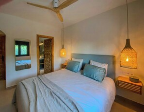 Quarto com cama, cabeceira de madeira, duas mesas de cabeceira, ventilador de teto e espelho.