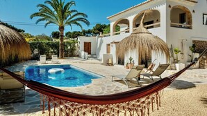 A pool with lounge chairs, a hammock, and a white building with arches. - Ibiza-style villa in Jávea near beach with pool (Jávea)