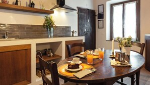 Zona pranzo con tavolo in legno, sedie e tavola imbandita per la colazione, con torta, caffè e succo d'arancia.