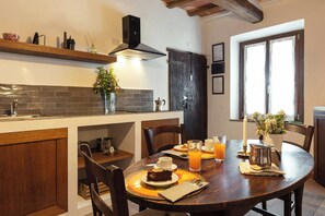 A dining area with a wooden table, chairs, and a breakfast setting including a cake, coffee, and orange juice. - Flat with pool in the Tuscan Maremma (Massa Marittima)