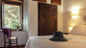 Una camera d'albergo con un letto, una sedia con un asciugamano viola, una porta di legno e una finestra con vista sugli alberi.
