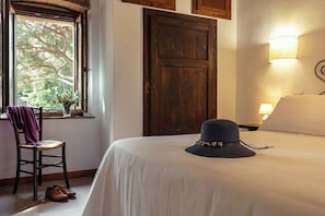 A hotel room with a bed, a chair with a purple towel, a wooden door, and a window with a view of trees. - Flat with pool in the Tuscan Maremma (Massa Marittima)