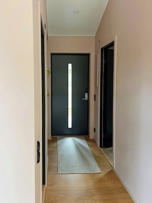 Un passadís amb una porta fosca, una paret de tons clars i un terra de fusta.