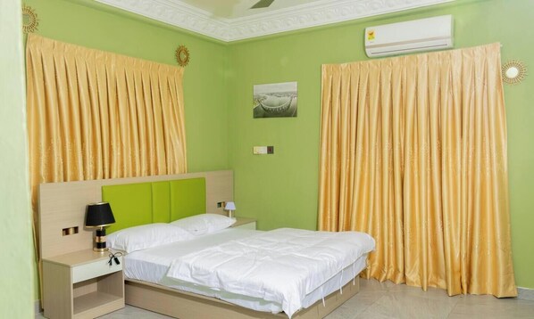 A room with a bed, nightstands, an air conditioner, and curtains.