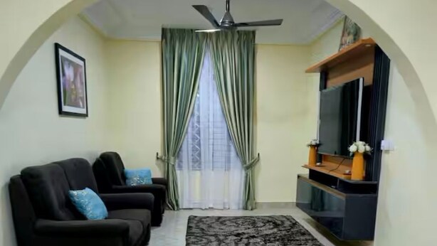 A living room with a sofa, a TV stand, a ceiling fan, and a window with curtains.