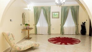 A living room with a floral armchair, a round red rug, and a table with a vase of flowers. - Modern 3BR Luxury Diamond Hills Residency (Kumasi)