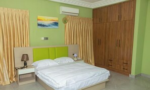 Une chambre à coucher comprenant un lit, une table de chevet, une lampe, un appareil de climatisation et une armoire.