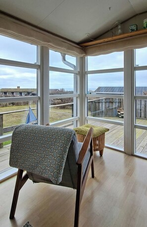 A room with large windows, a wooden bench, a small table, and a view of the outdoors. - Cozy yellow holiday home with sea view (Slagelse)