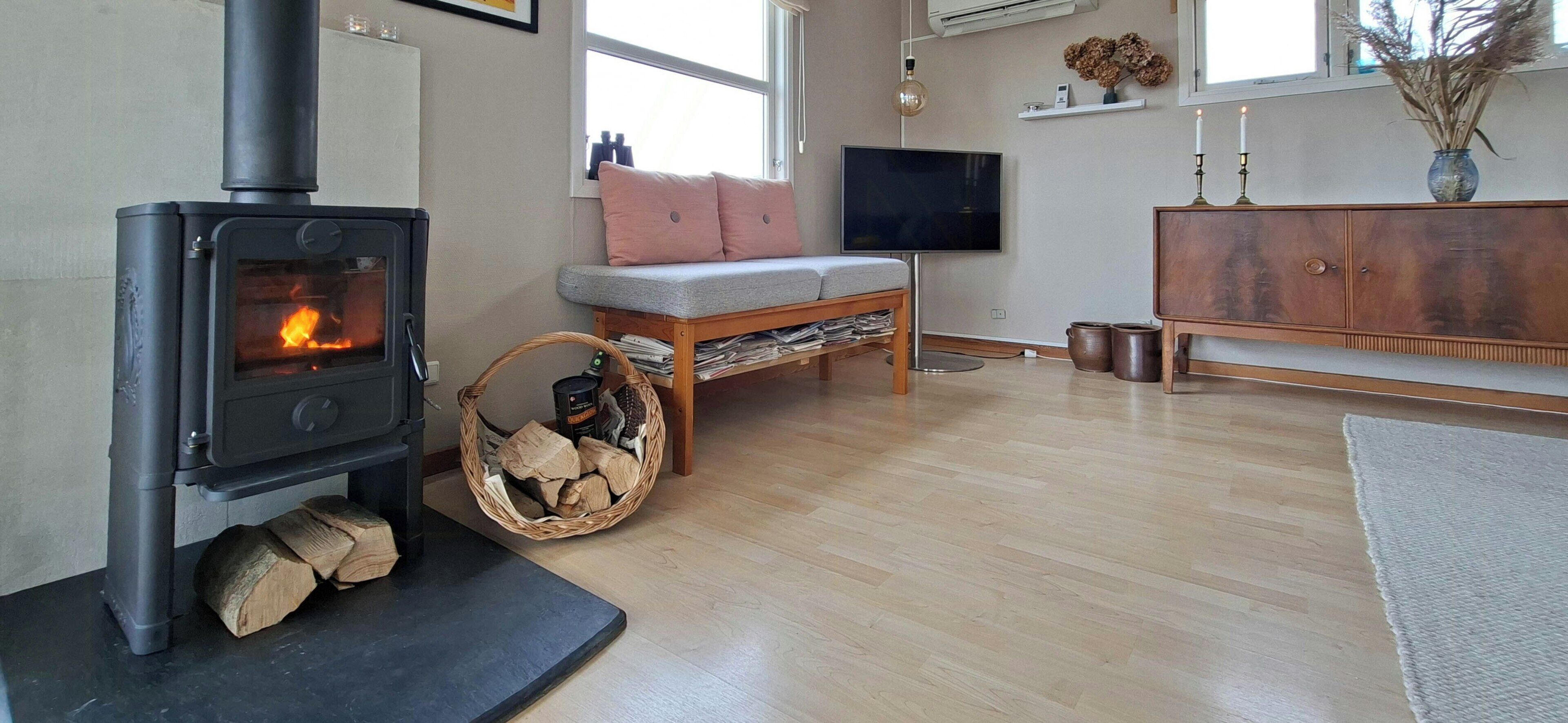 A cozy living room with a wood-burning stove, a comfortable sofa, a flat-screen TV, and a wooden cabinet.