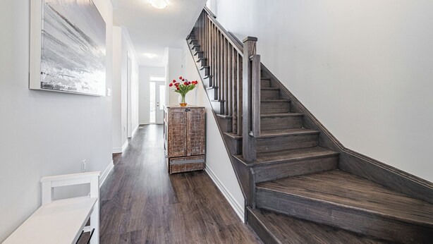 Een modern interieur met een houten trap, een witte muur met een schilderij en een vaas met rode bloemen op een houten kast.