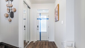 Een hal met een houten vloer, een bankje, een deur versierd met een blauw lint, en een kunstwerk aan de muur.