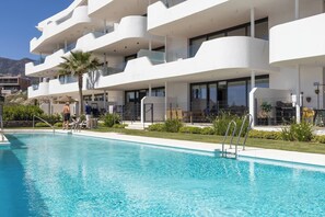 A modern hotel with a swimming pool, multiple balconies, and a view of the mountains. - Exclusive Garden Suite in Higueron (Fuengirola)