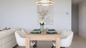 A dining area with a wooden table, white chairs, a vase with flowers, and a pendant light. - Exclusive Garden Suite in Higueron (Fuengirola)