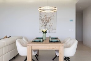 A dining area with a wooden table, white chairs, a vase with flowers, and a pendant light. - Exclusive Garden Suite in Higueron (Fuengirola)