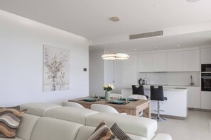 Uma sala de estar moderna com sofá, mesa de jantar e cadeiras. Há uma cozinha com armários brancos e uma mesa de jantar.