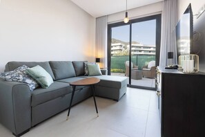 A modern living room with a grey sectional sofa, a small round table, and a dark wooden cabinet with a TV and decorative items. - Exclusive Garden Suite in Higueron (Fuengirola)