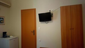 Een kamer met een houten deur, een klein tafeltje, een aan de muur bevestigde televisie en een wit apparaat.