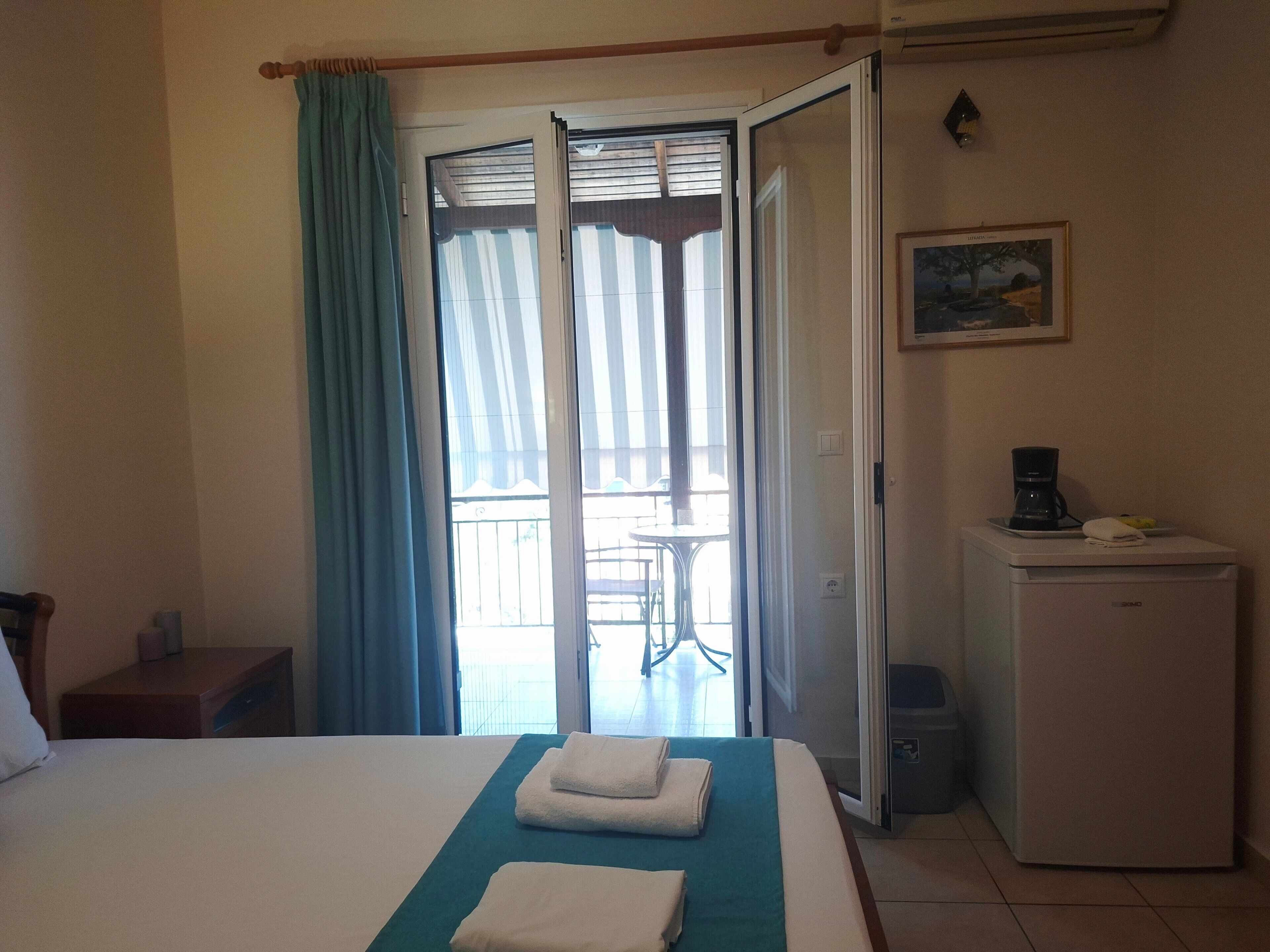 Ein Hotelzimmer mit Bett, Schreibtisch, Kühlschrank, Kaffeemaschine und einem Balkon mit Aussicht.