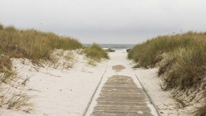 Polku, joka johtaa rannalle, ja jonka molemmilla puolilla on hiekkaa ja ruohoa.