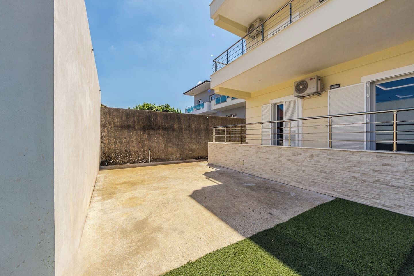 A modern building with a flat roof, a concrete wall, and a small grassy area.