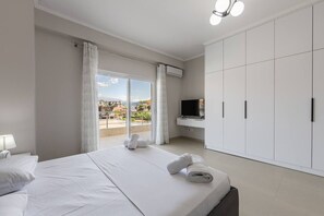 Habitación de hotel con cama, televisión, armario y balcón con vistas.