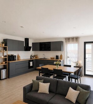A modern kitchen with dark cabinets, a wooden dining table, and a sofa in the living area. - Just outside Colmar and the vineyards—On-site EV Charging (Ingersheim)