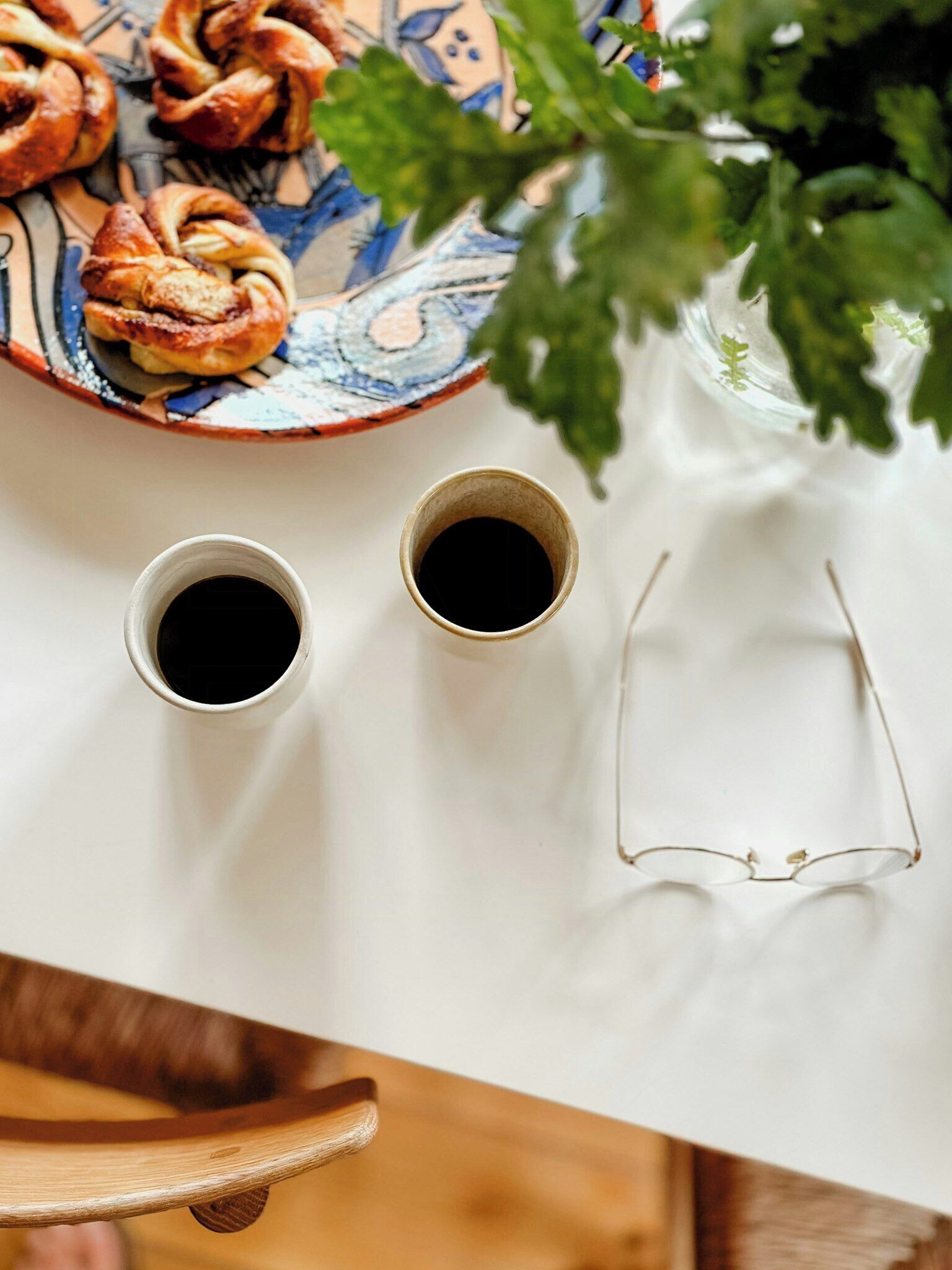 Et bord med to kopper kaffe, et par briller og et fad med kager.