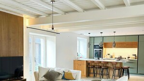 Una sala moderna con un sofá, una mesa de centro y un televisor. Se ve una cocina con taburetes de bar y una zona de comedor al fondo.