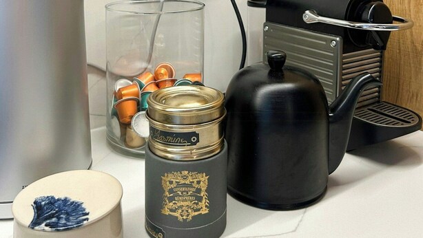 Una encimera de cocina con un hervidor, un tarro de vidrio, un recipiente con tapas y una cafetera.