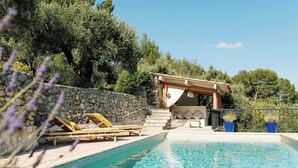A pool area with lounge chairs, a stone wall, and a pergola. - Exceptional apartment in Cannes' countryside (Spéracèdes)