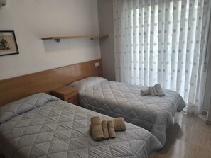 A hotel room with two beds, a wooden headboard, a bedside table, and a window with sheer curtains. - Larimar Family & Leisure Center (Salou)