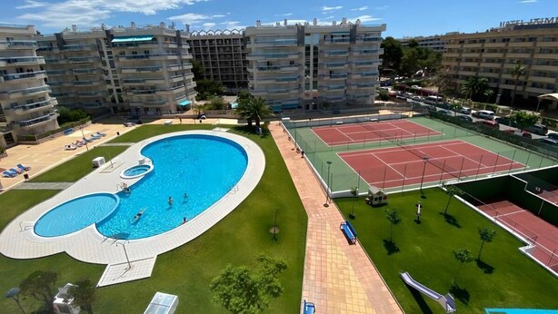 Un edifici residencial amb nombroses balconades, una piscina, pistes de tenis i un jardí ben cuidat.