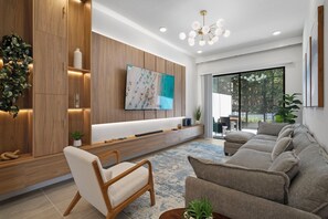 Un salon moderne avec un canapé, un meuble en bois, un téléviseur et un luminaire fixé au plafond.